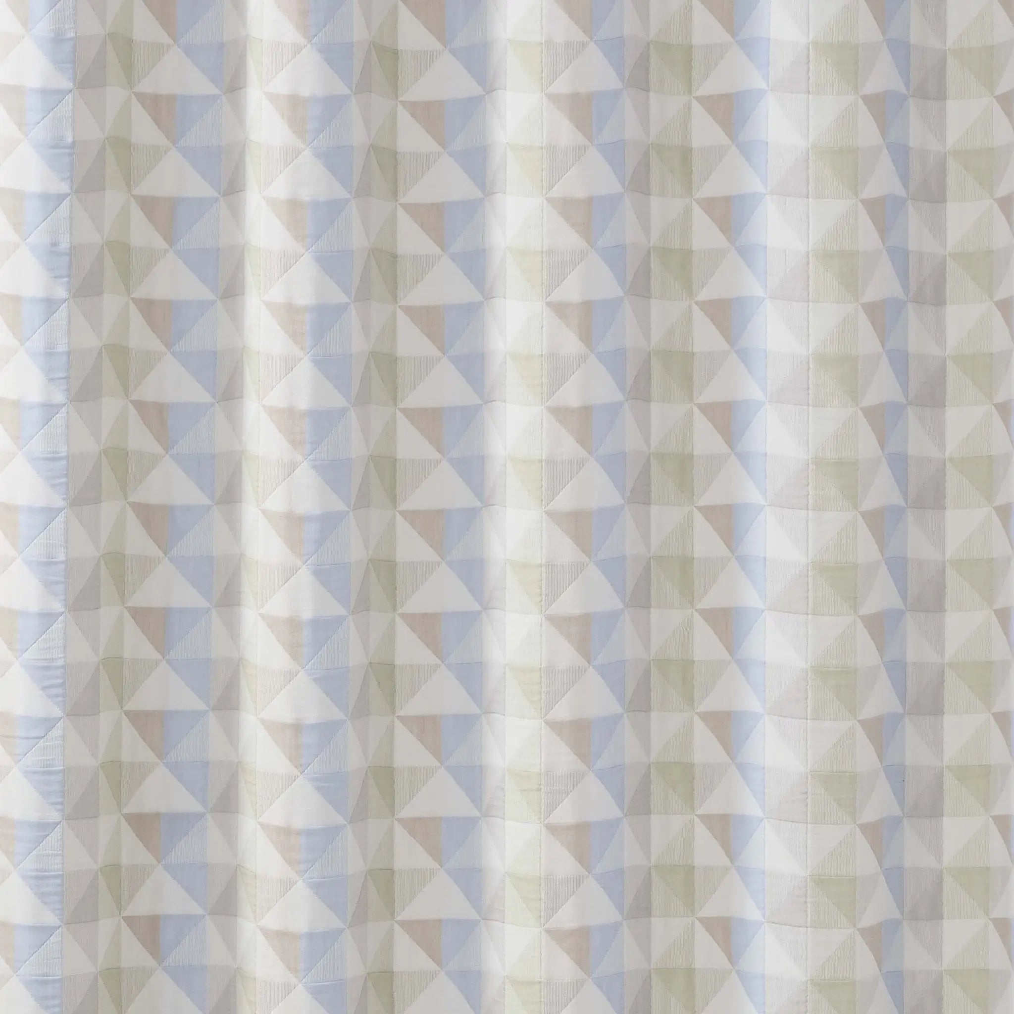 A close-up of a fabric surface with a repeating geometric triangle pattern in soft off-white, pale blue, and muted beige.
