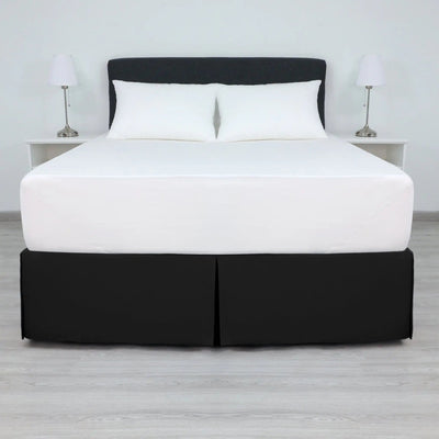 A bed with a white mattress and two white pillows, dressed in a black bed skirt.