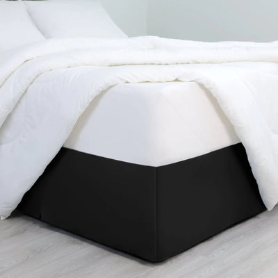 A bed dressed in white bedding, with a black bed skirt covering the base of the frame.