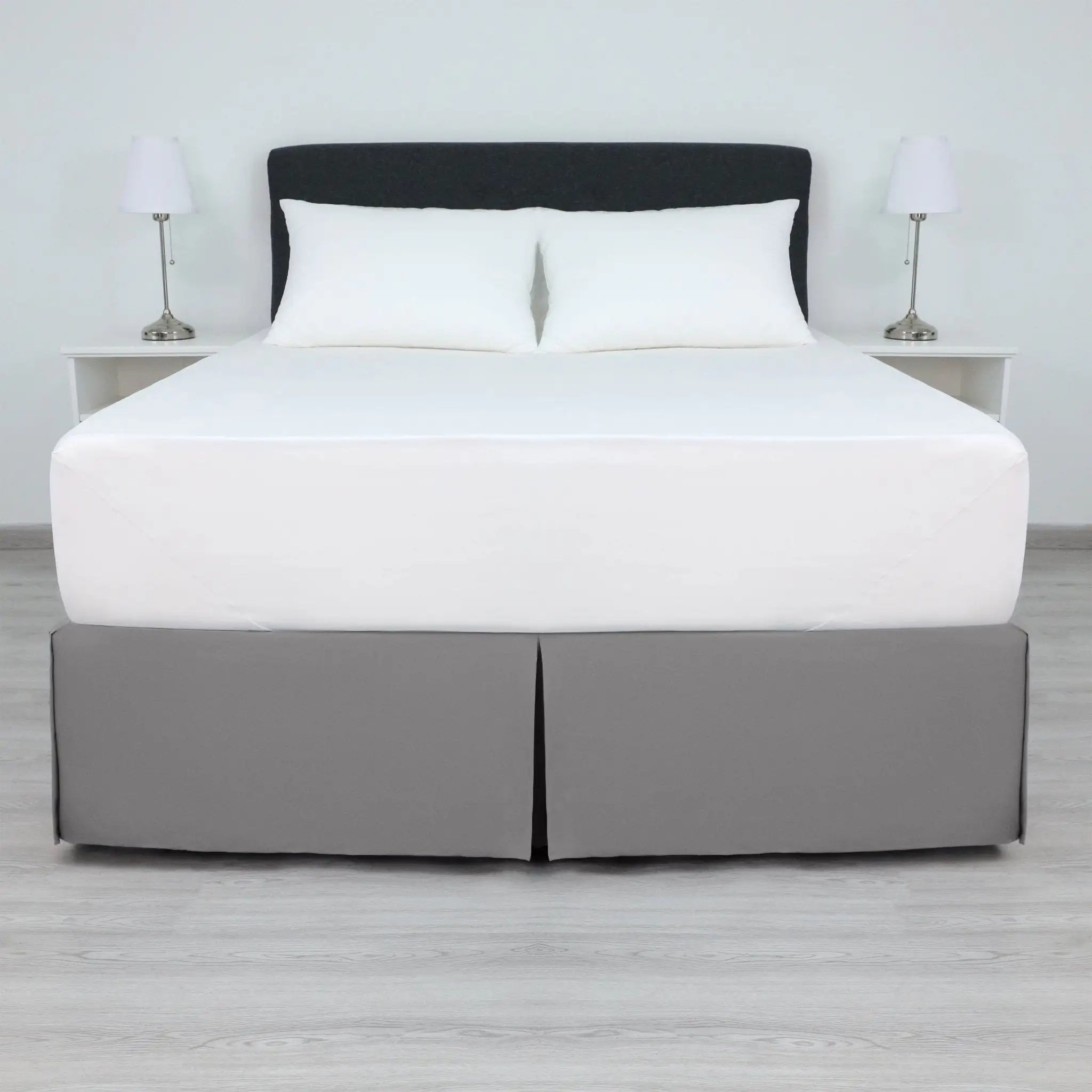 A bed with a white mattress and two white pillows, dressed in a gray bed skirt.