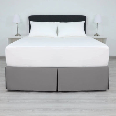 A bed with a white mattress and two white pillows, dressed in a gray bed skirt.