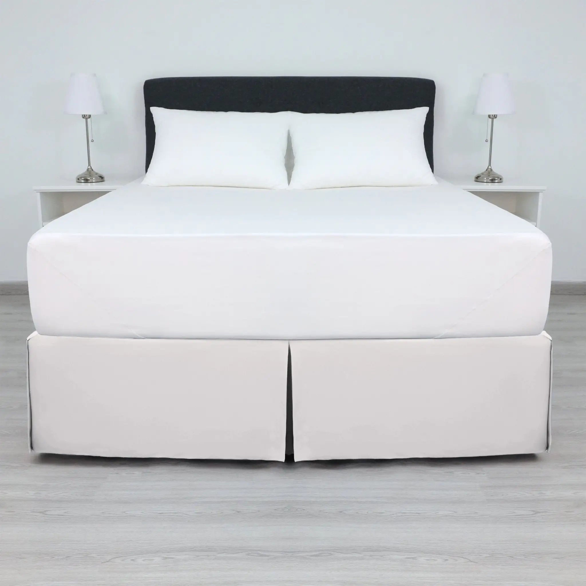 A bed with a white mattress and two white pillows, dressed in a white bed skirt.