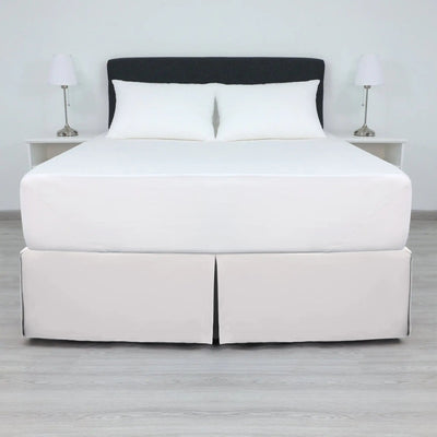 A bed with a white mattress and two white pillows, dressed in a white bed skirt.