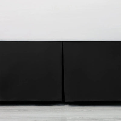 Close-up of a black bed skirt with a white base on a light wood floor.