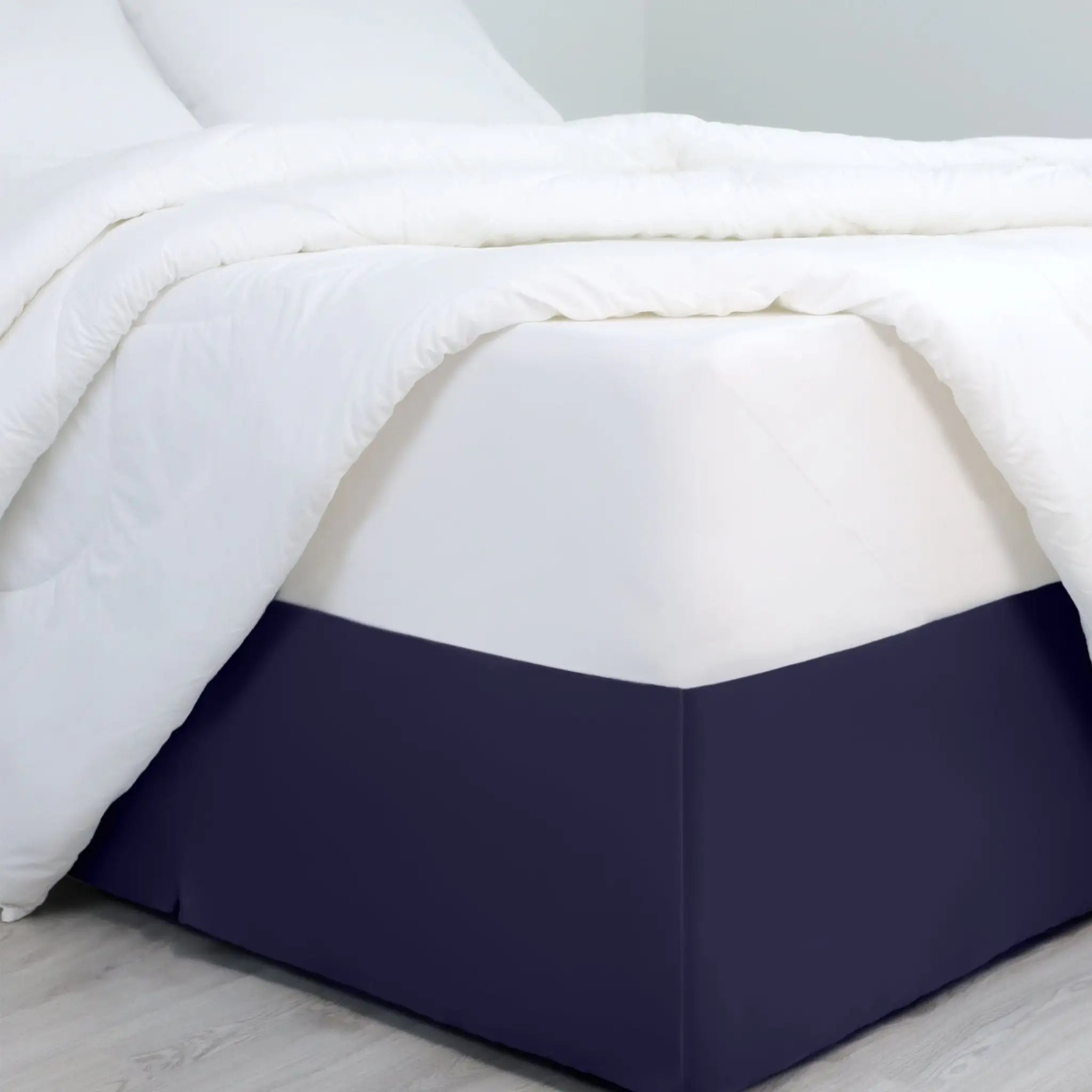 A bed dressed in white bedding, with a navy bed skirt covering the base of the frame.