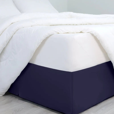 A bed dressed in white bedding, with a navy bed skirt covering the base of the frame.