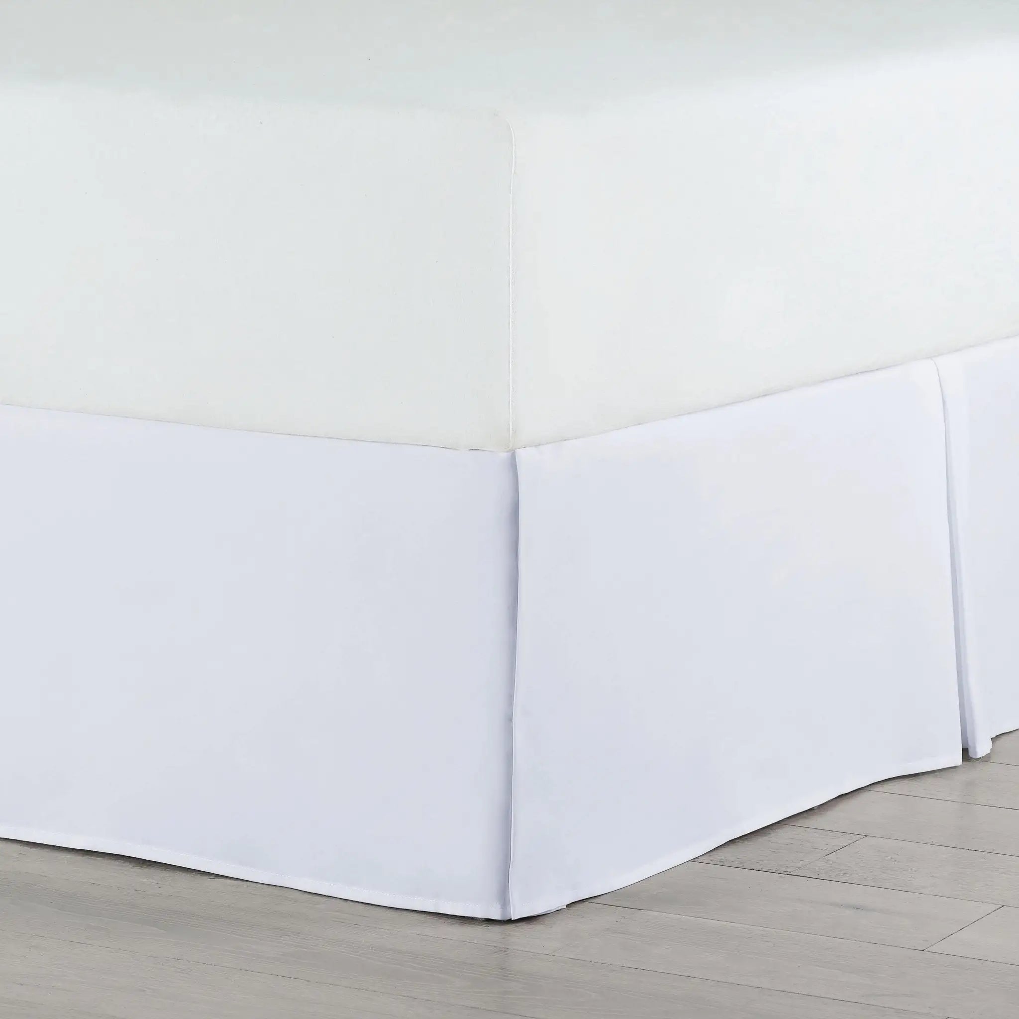 A white bed skirt fitted around the base of a bed, shown in a clean room setting with light wood flooring.