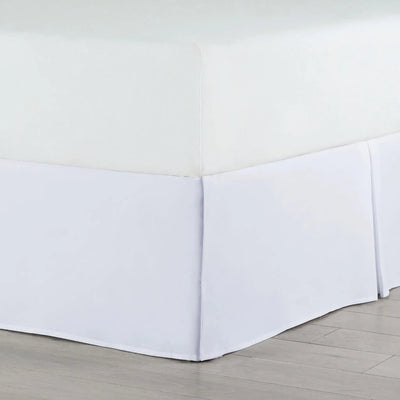 A white bed skirt fitted around the base of a bed, shown in a clean room setting with light wood flooring.