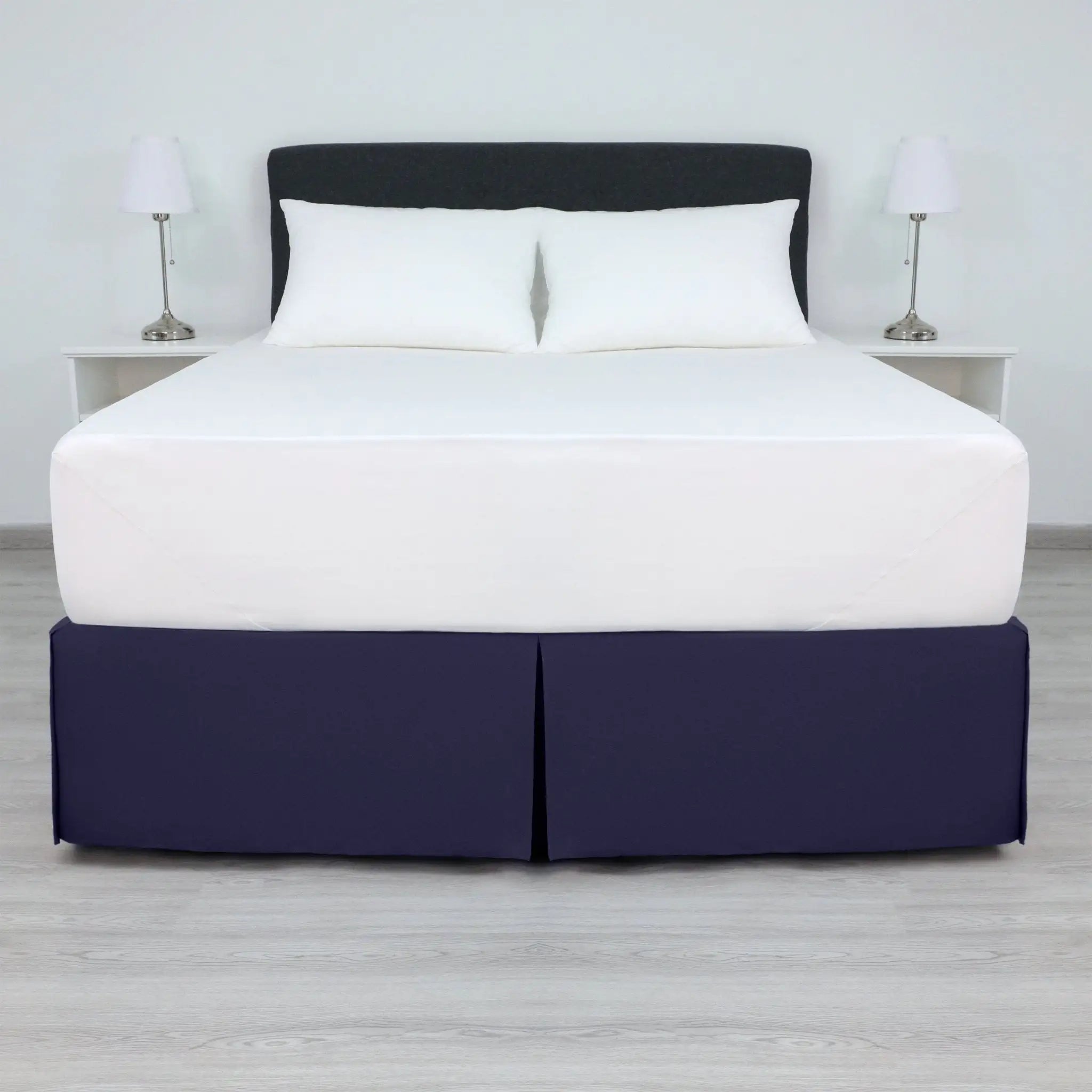 A bed with a white mattress and two white pillows, dressed in a navy bed skirt.