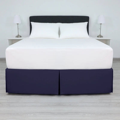 A bed with a white mattress and two white pillows, dressed in a navy bed skirt.