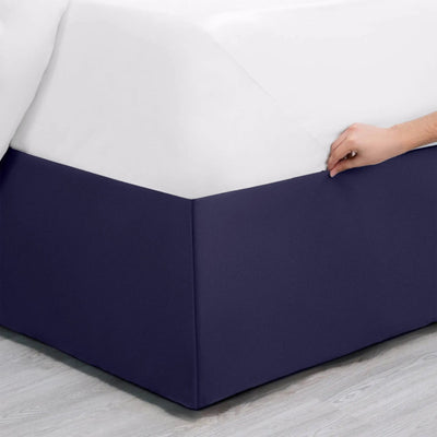 Navy bed skirt being adjusted on a bed with a white mattress.