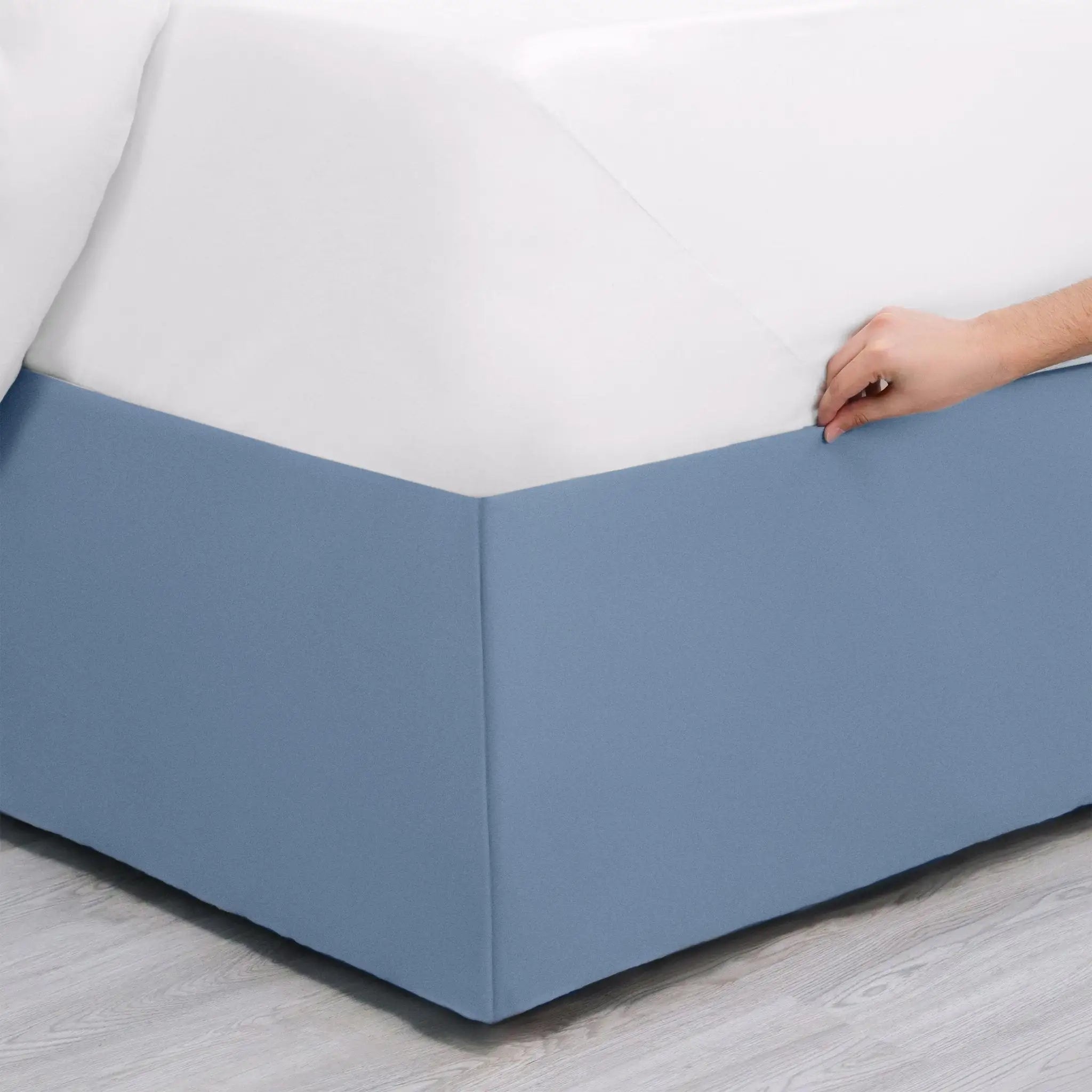 Blue bed skirt being adjusted on a bed with a white mattress.