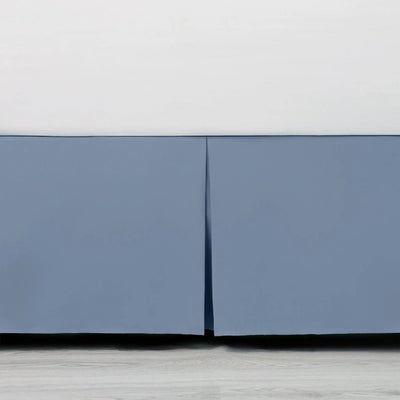 Close-up of a blue bed skirt with a white base on a light wood floor.