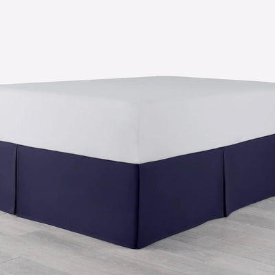 A bed with a fitted white sheet and a navy bed skirt, shown in a setting with light gray flooring.