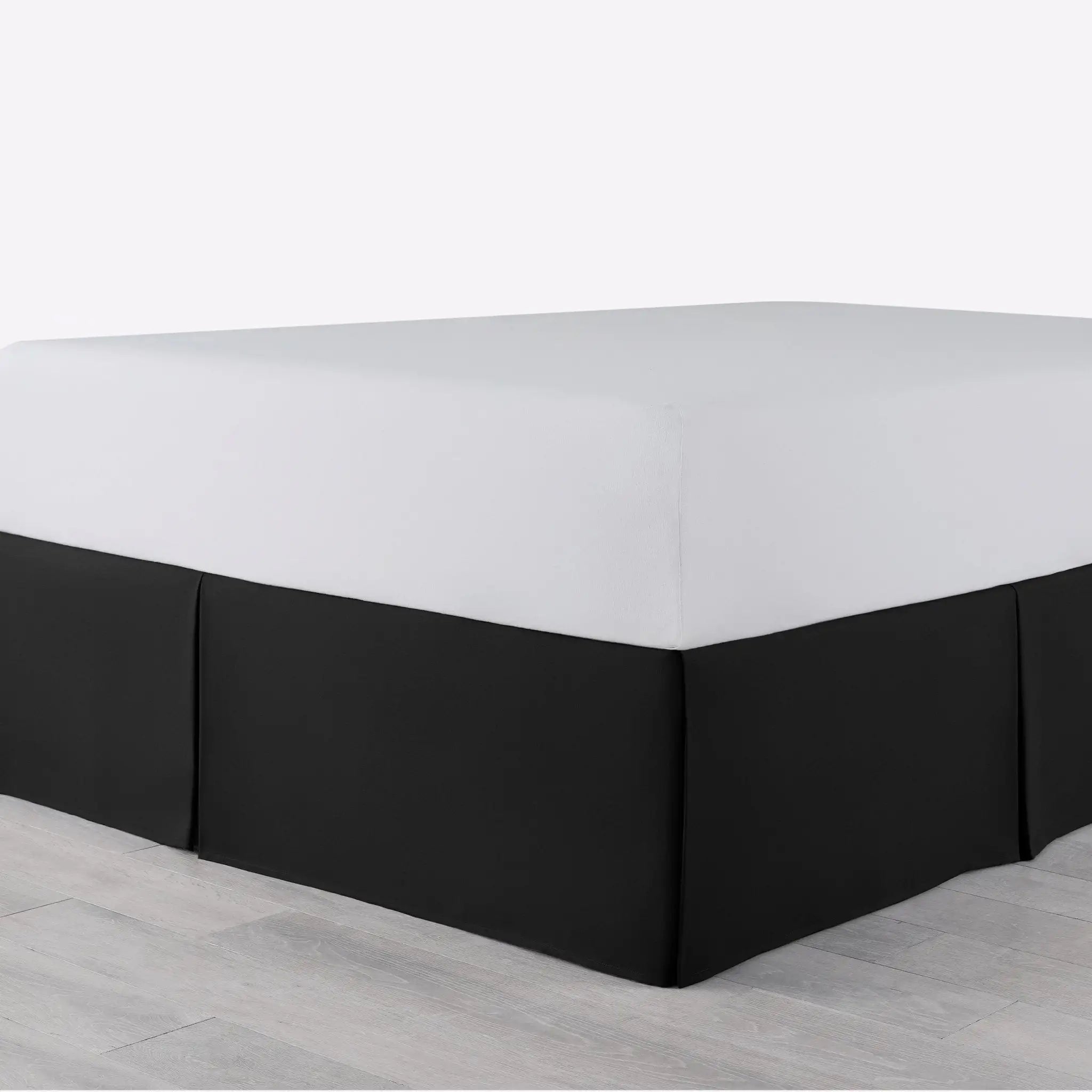 A bed with a fitted white sheet and a black bed skirt, shown in a setting with light gray flooring.