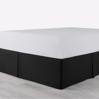 A bed with a fitted white sheet and a black bed skirt, shown in a setting with light gray flooring.
