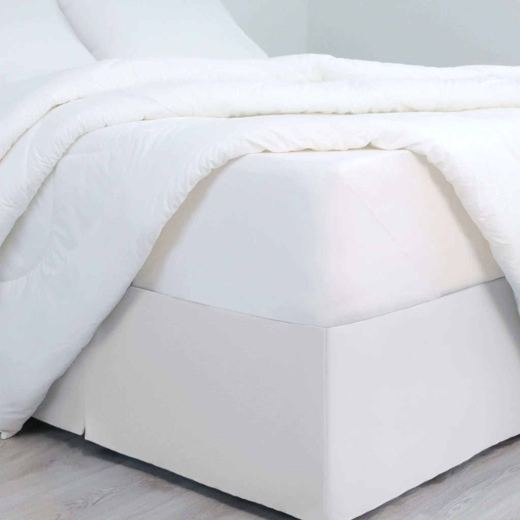A bed dressed in white bedding, with a white bed skirt covering the base of the frame.