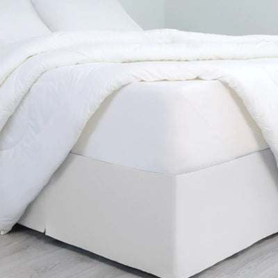 A bed dressed in white bedding, with a white bed skirt covering the base of the frame.