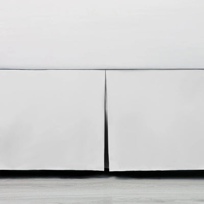 Close-up of a white bed skirt with a white base on a light wood floor.