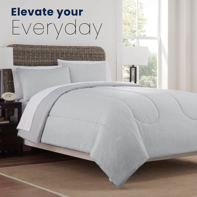 Gray comforter set on a bed in a bedroom with text 'Elevate your Everyday'.