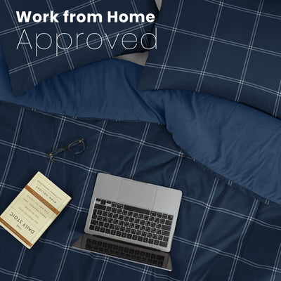 Navy checkered bedding with a laptop, glasses, and notebook on a bed.