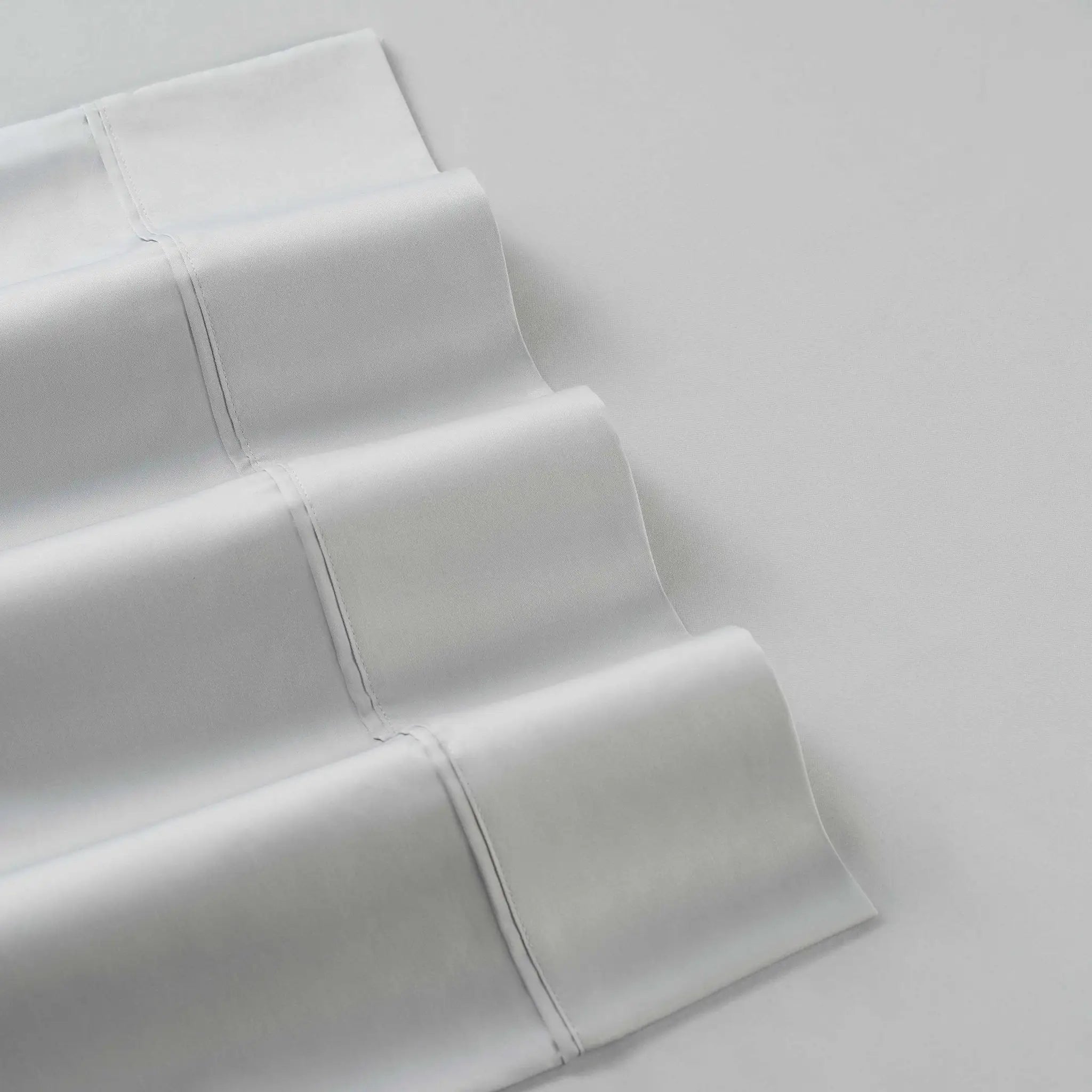 A close-up of folded white fabric with visible stitched paneling, photographed on a light gray background.