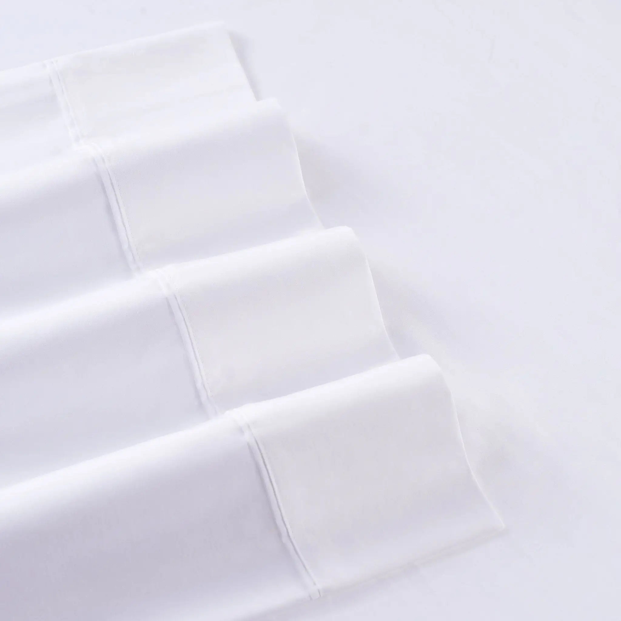 White folded fabric with a subtle woven texture, arranged diagonally on a matching white background.