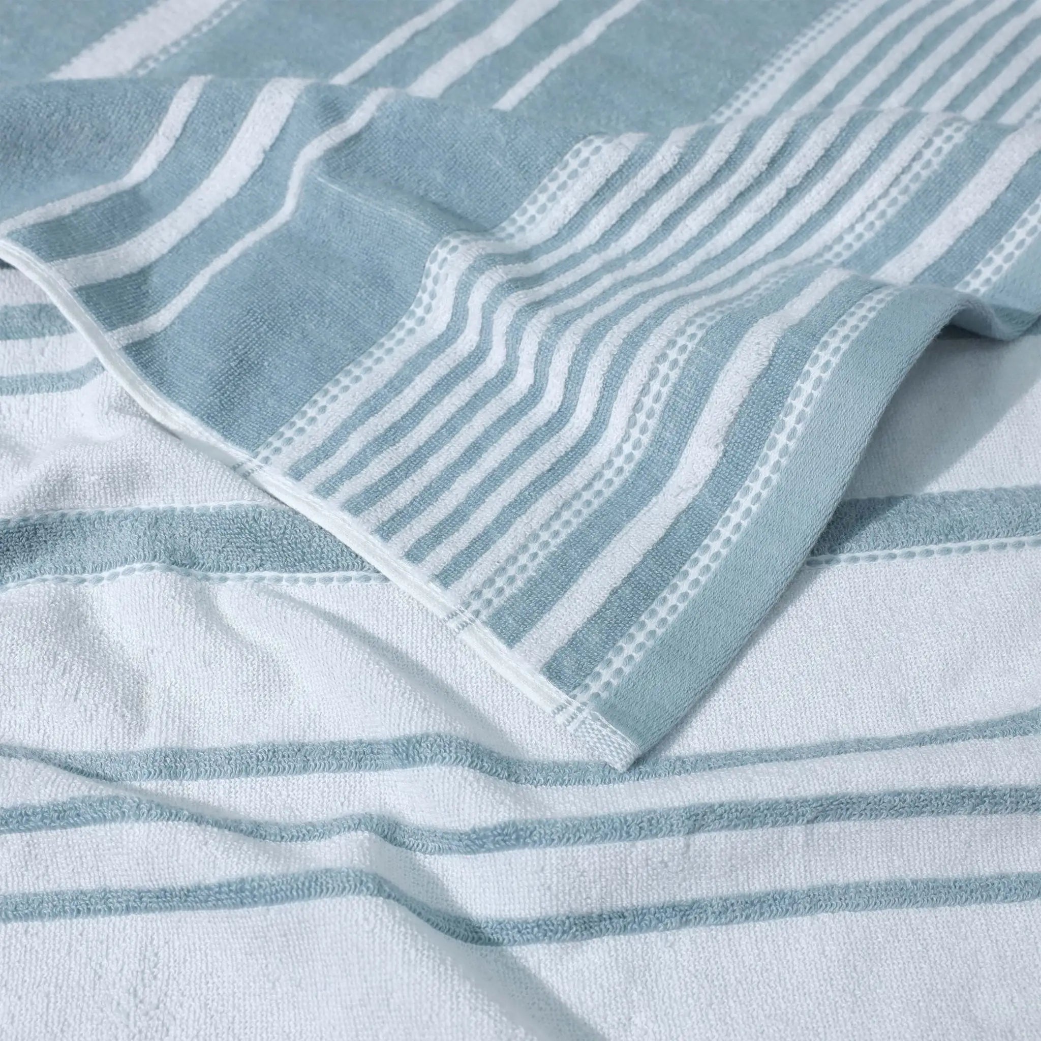 A close-up of a striped, mineral colored towel textile and a folded corner showing the fabric texture.