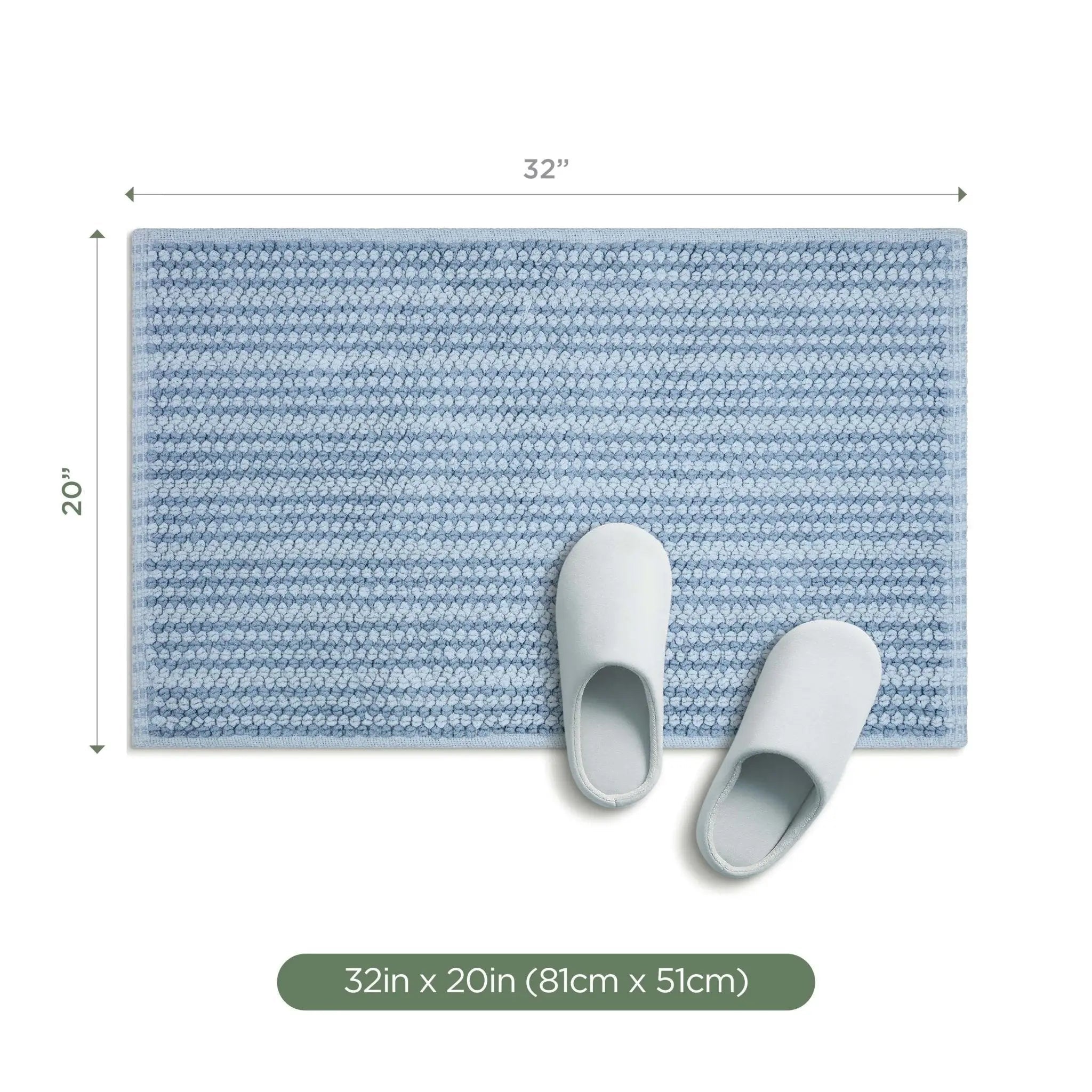 A rectangular blue textured bath rug shown on a white background with dimension arrows indicating 32 inches by 20 inches, plus two white slippers placed on the mat.