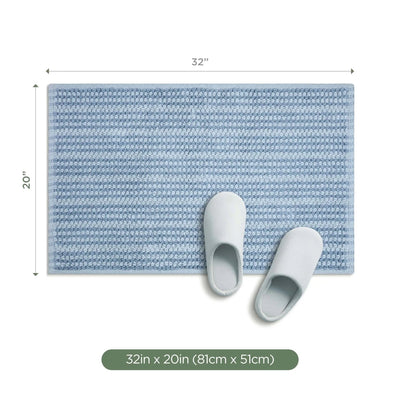 A rectangular blue textured bath rug shown on a white background with dimension arrows indicating 32 inches by 20 inches, plus two white slippers placed on the mat.