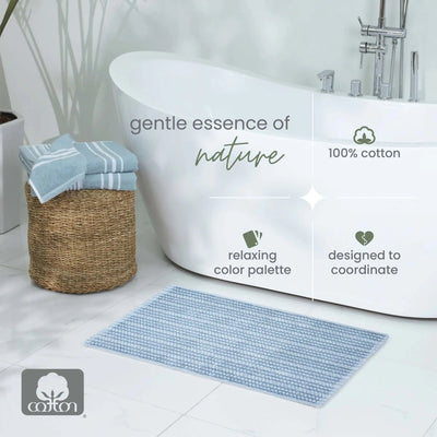 A blue bath mat in a bright bathroom setting next to a white freestanding bathtub, with overlaid text reading 'gentle essence of nature', '100% cotton', 'relaxing color palette', and 'designed to coordinate'.