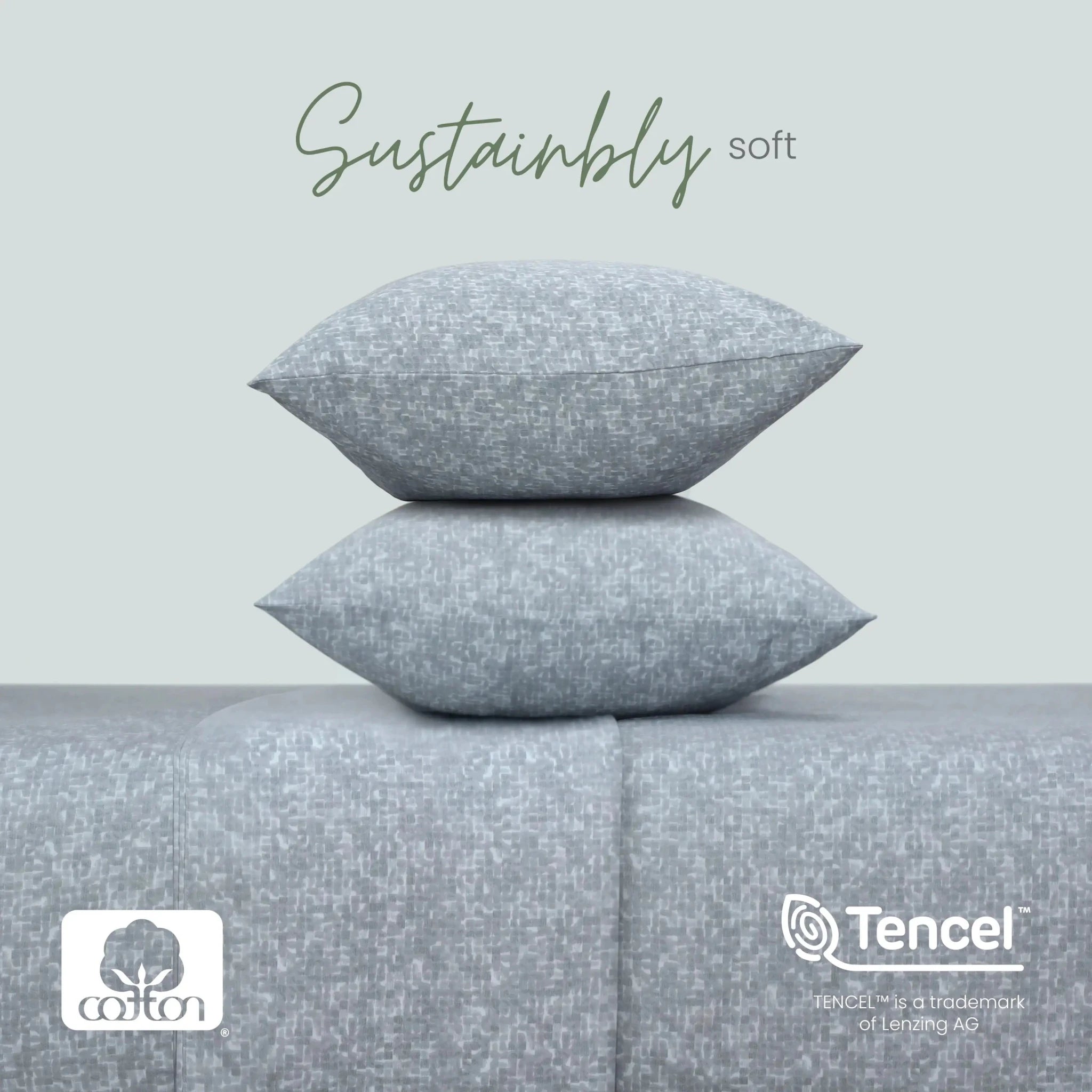 Two light gray textured pillows stacked on a matching gray upholstered surface, with the words 'Sustainably soft' above. Cotton and Tencel logos appear at the bottom, with a pale gray background.