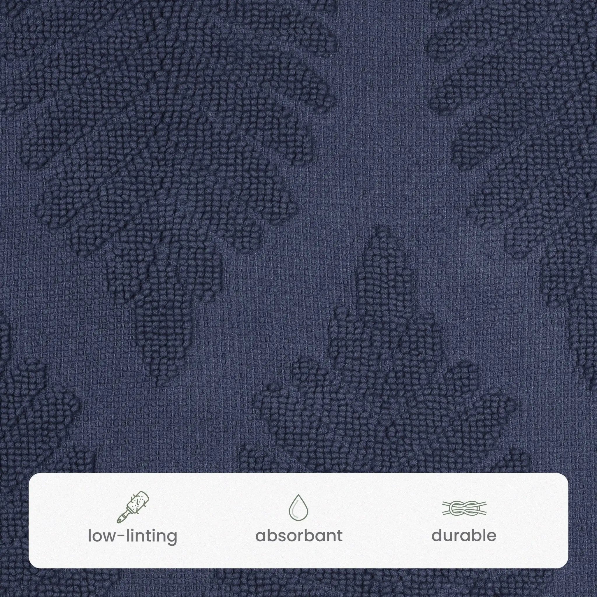 Close-up of a navy textured fabric with a subtle tonal leaf pattern, featuring a white informational strip at the bottom with icons and the words low-linting, absorbant, and durable.