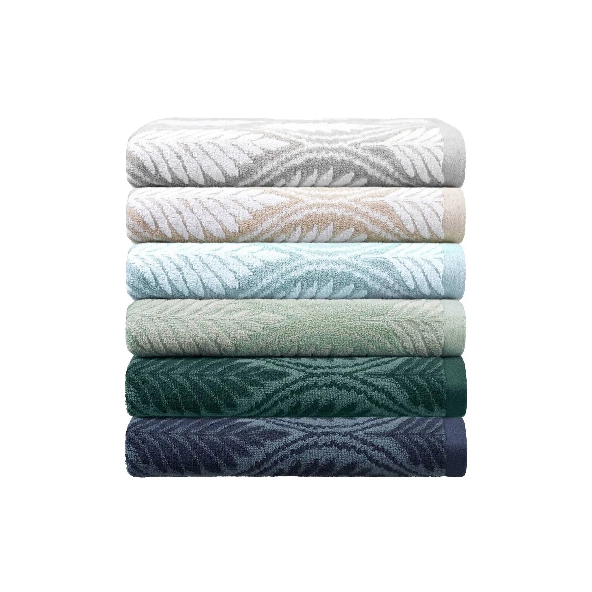 A stack of six folded bath towels with a textured leaf pattern, shown in a gradient of colors from light gray and white to sage green, teal, forest green, and navy blue, on a solid white background.