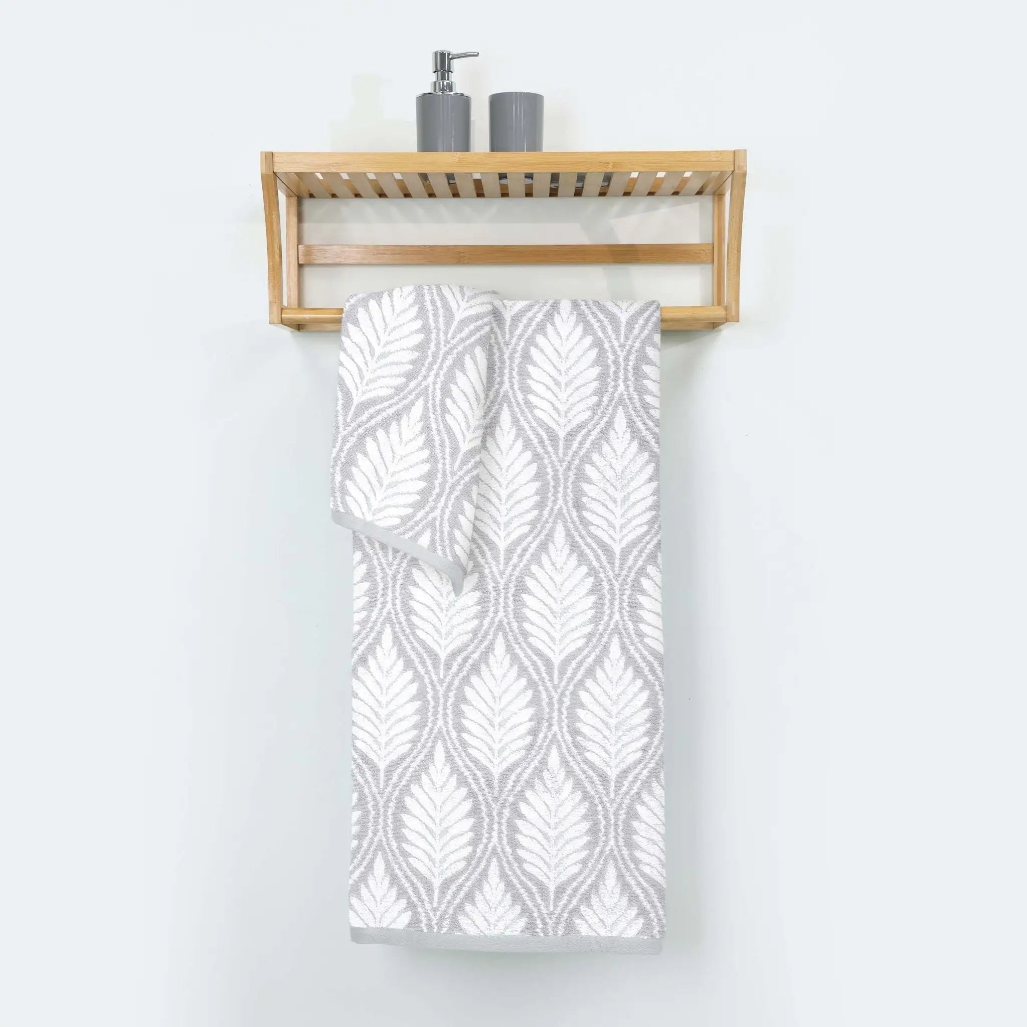 Grey patterned bath towel hanging on a wooden towel rack against a white wall.