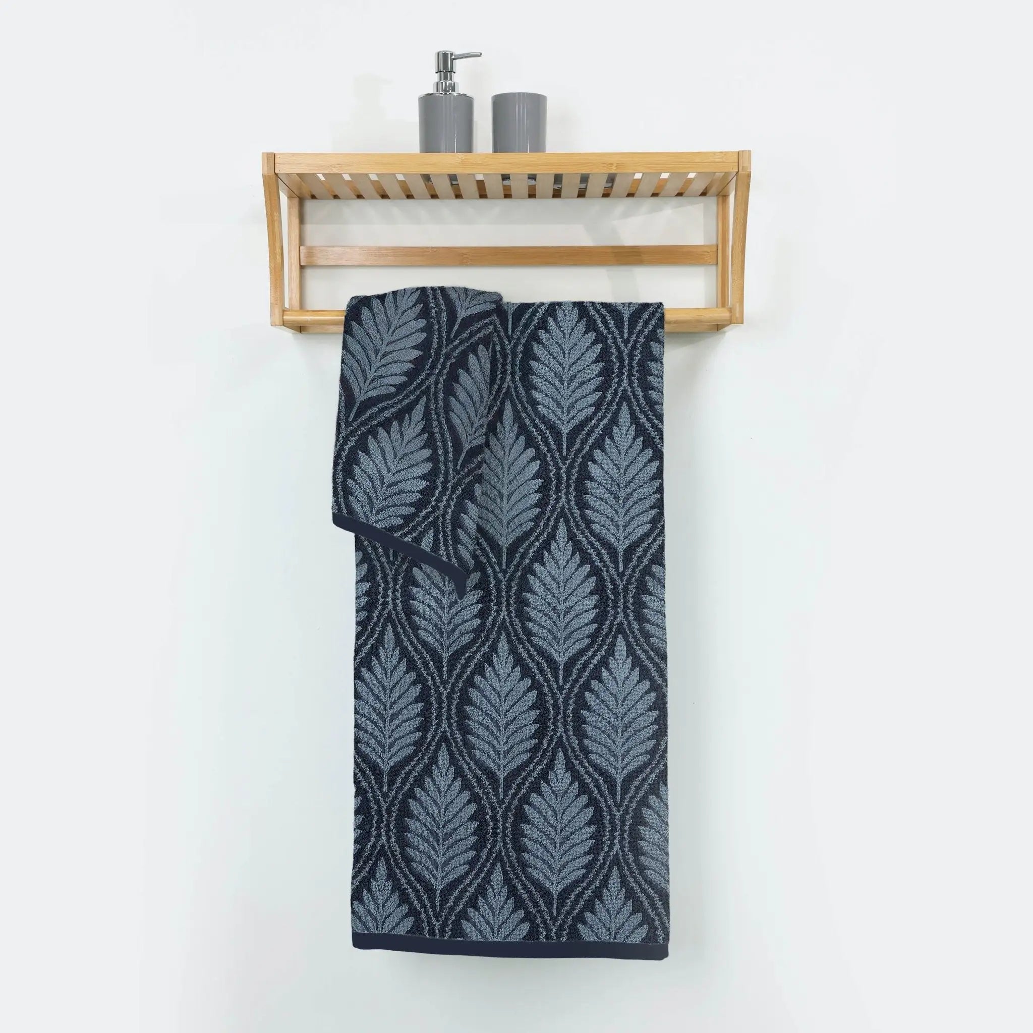 A navy bath towel with a leaf pattern hangs from a light wood wall-mounted shelf.