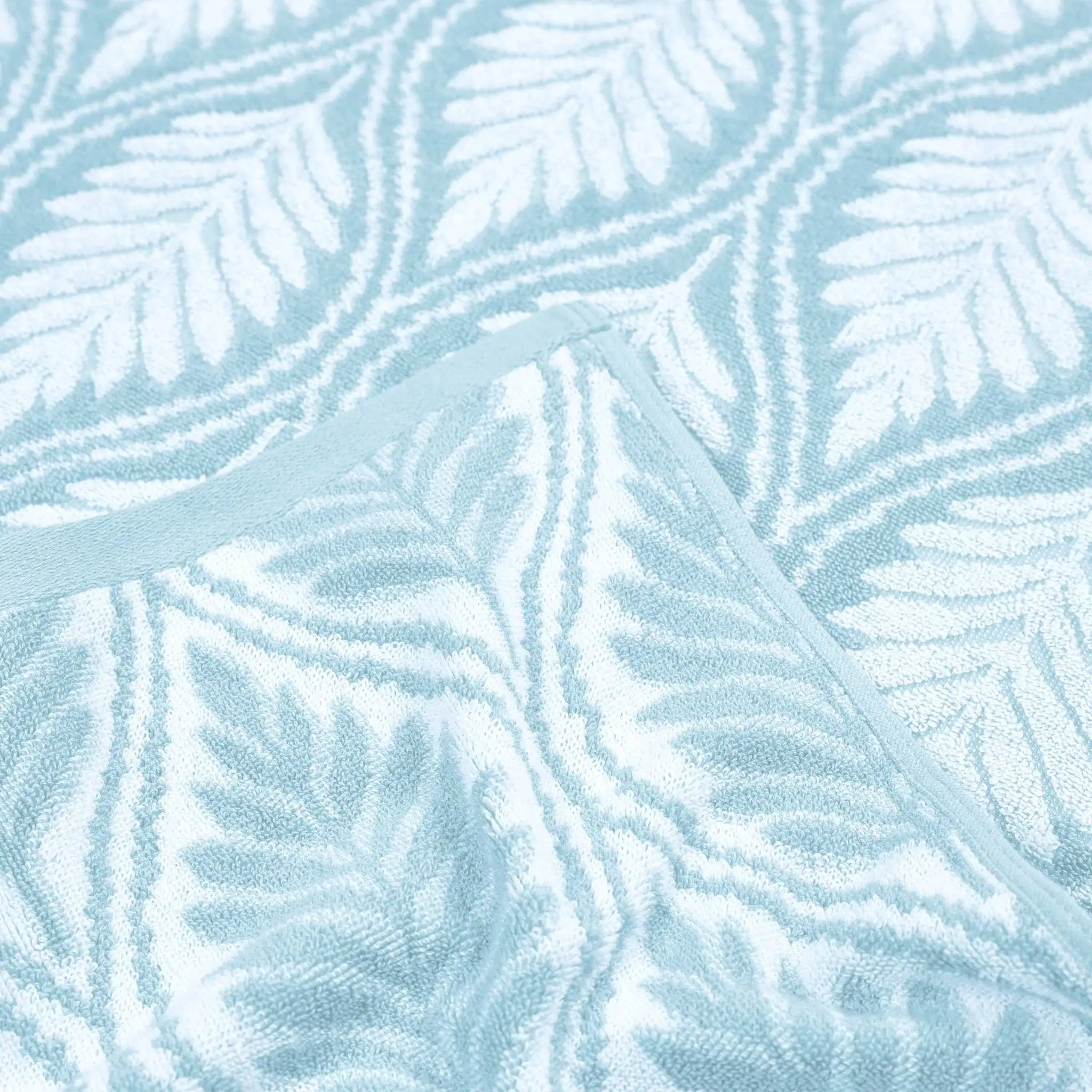 A close-up of a light blue and white textured fabric with an embossed leaf pattern and a stitched border.