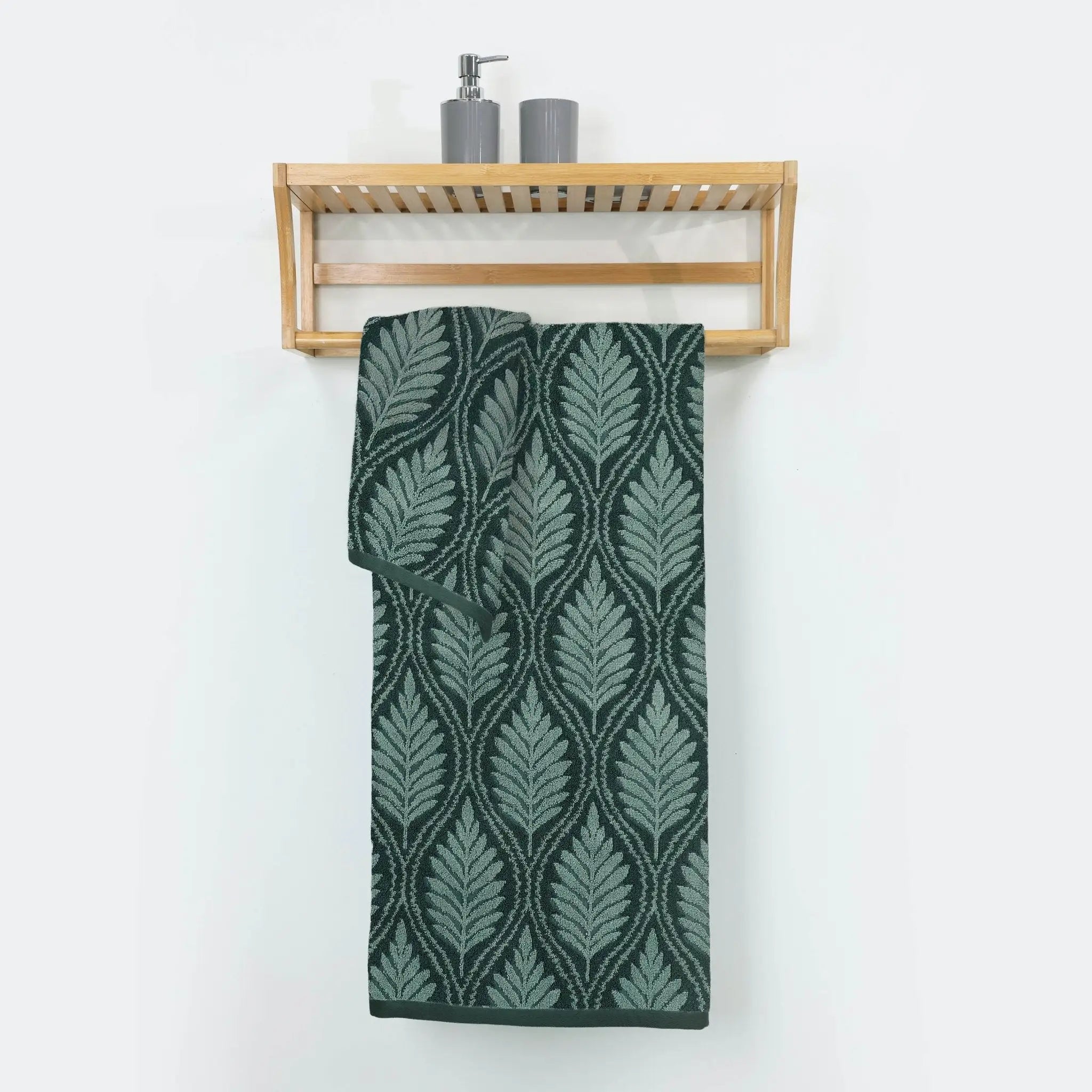 A Jade bath towel with a repeating light green leaf pattern hangs from a light wood wall-mounted towel rack.