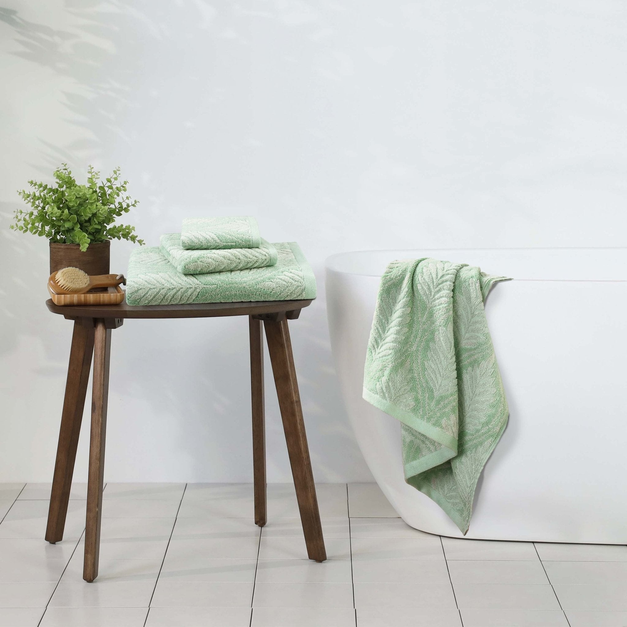 sage towels on a wooden stool with a plant against a white wall.
