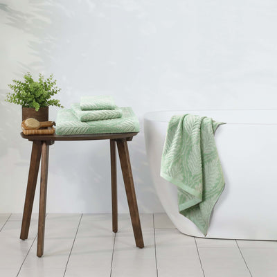 sage towels on a wooden stool with a plant against a white wall.