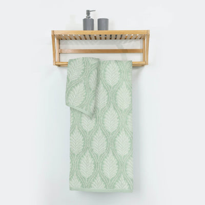 Sage patterned towel hanging on a wooden towel rack against a white wall.