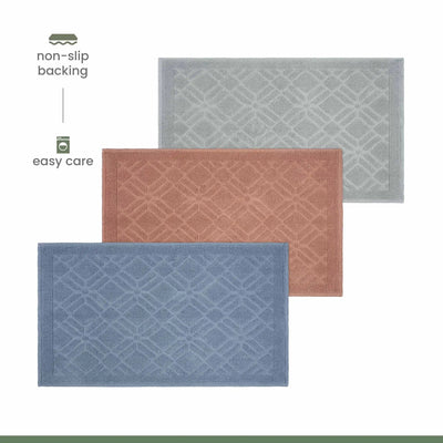 Three rectangular bath rugs with a raised geometric pattern are shown on a white background, labeled with features: non-slip backing and easy care. The mats are in blue, dusty rose, and light gray, arranged diagonally.