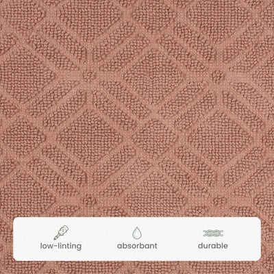Close-up of a textured fabric surface in a clay colored bath rug, with a white banner at the bottom containing small icons and the words low-linting, absorbant, and durable.
