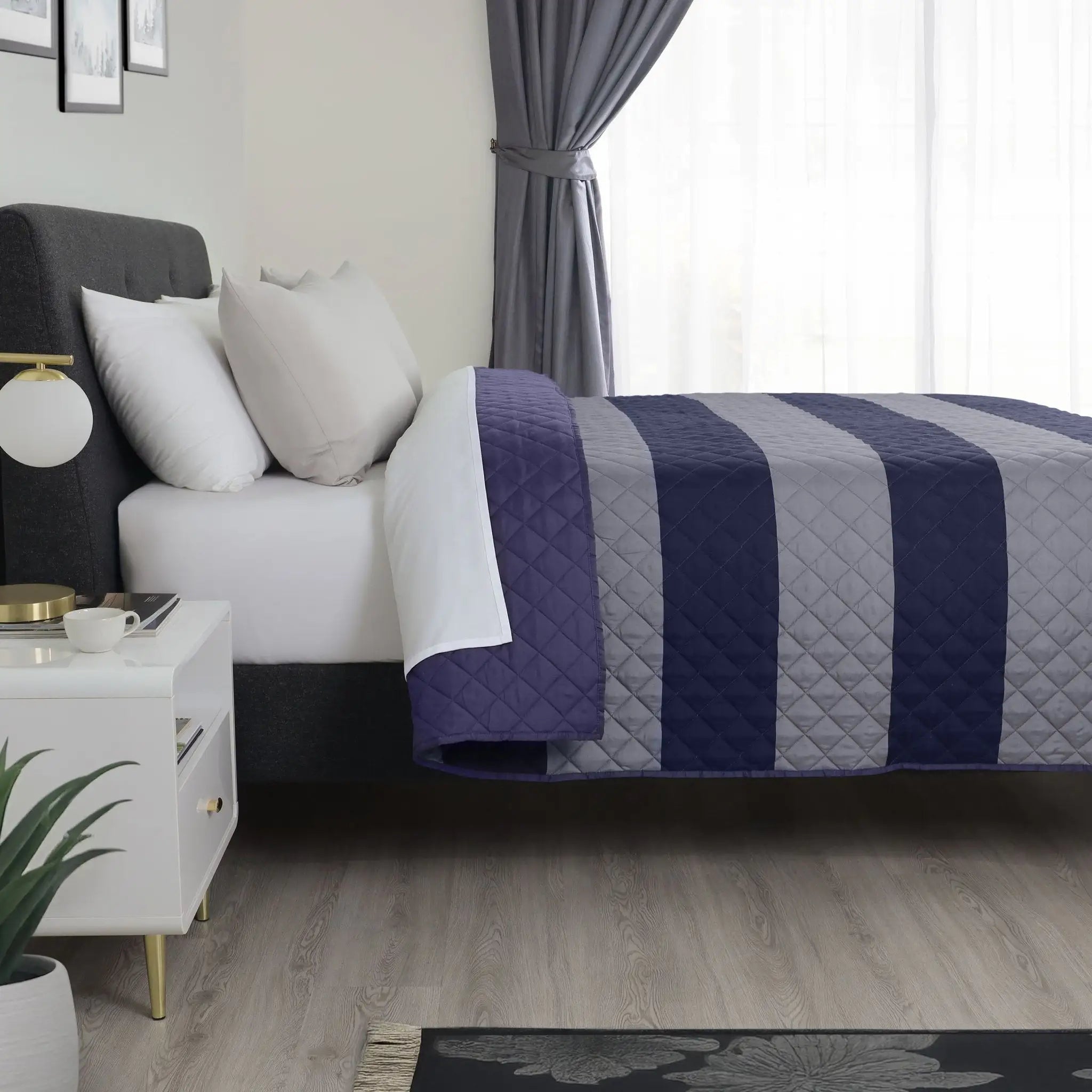 A bed dressed in a quilted striped coverlet with navy blue and light gray vertical bands.