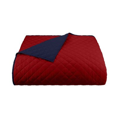 A folded quilted coverlet in deep red with a navy-blue reverse side, shown on a plain white background.