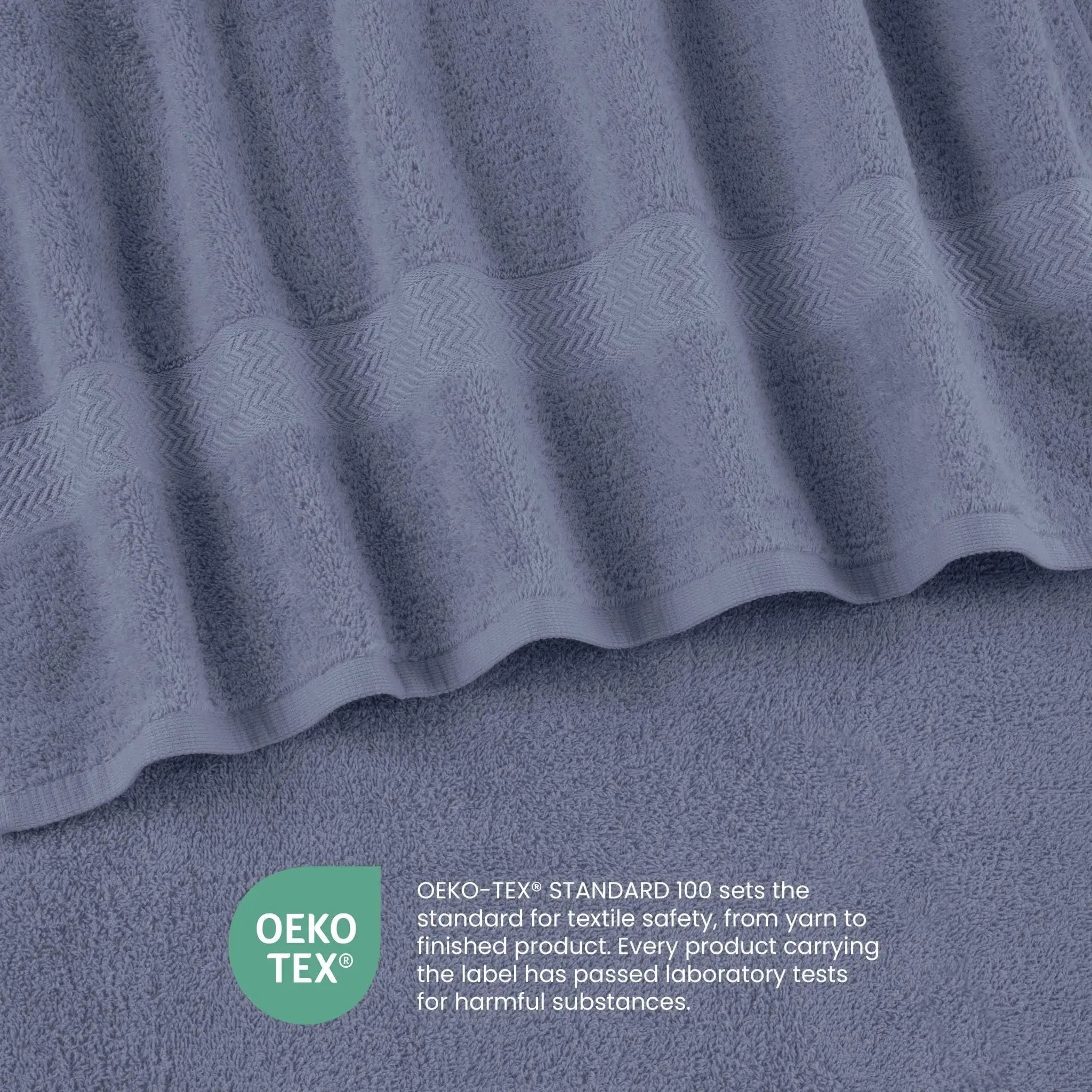 A close-up of a heather blue textured towel with a wavy patterned border, shown with an OEKO-TEX certification badge and text overlay at the bottom.