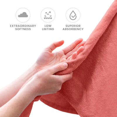 Person holding a coral towel with icons and text indicating softness, low linting, and absorbency.