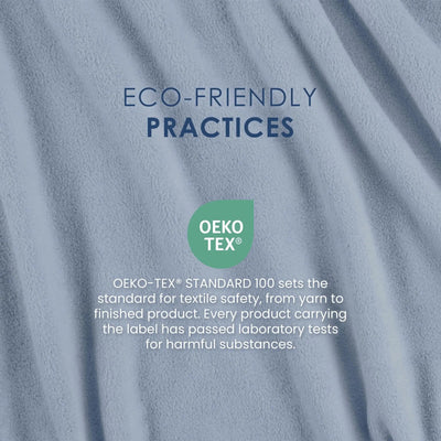 A close-up of soft blue-gray fabric with draped folds and printed text reading 'ECO-FRIENDLY PRACTICES' and an OEKO-TEX badge, explaining textile safety standards.