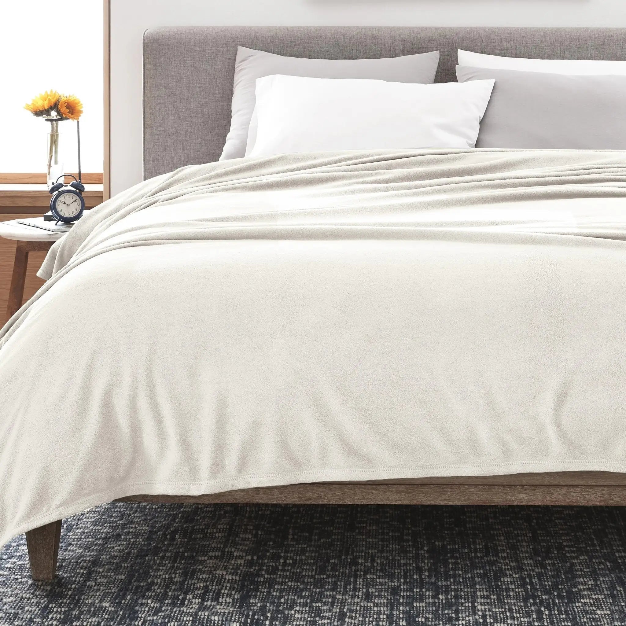 Neatly made bed with ivory blanket in a bedroom setting.