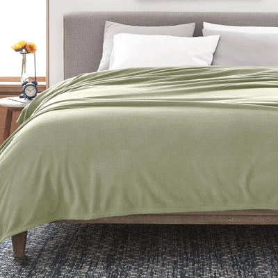 A sage green blanket draped over a bed with white and gray pillows, shown in a styled bedroom setting.